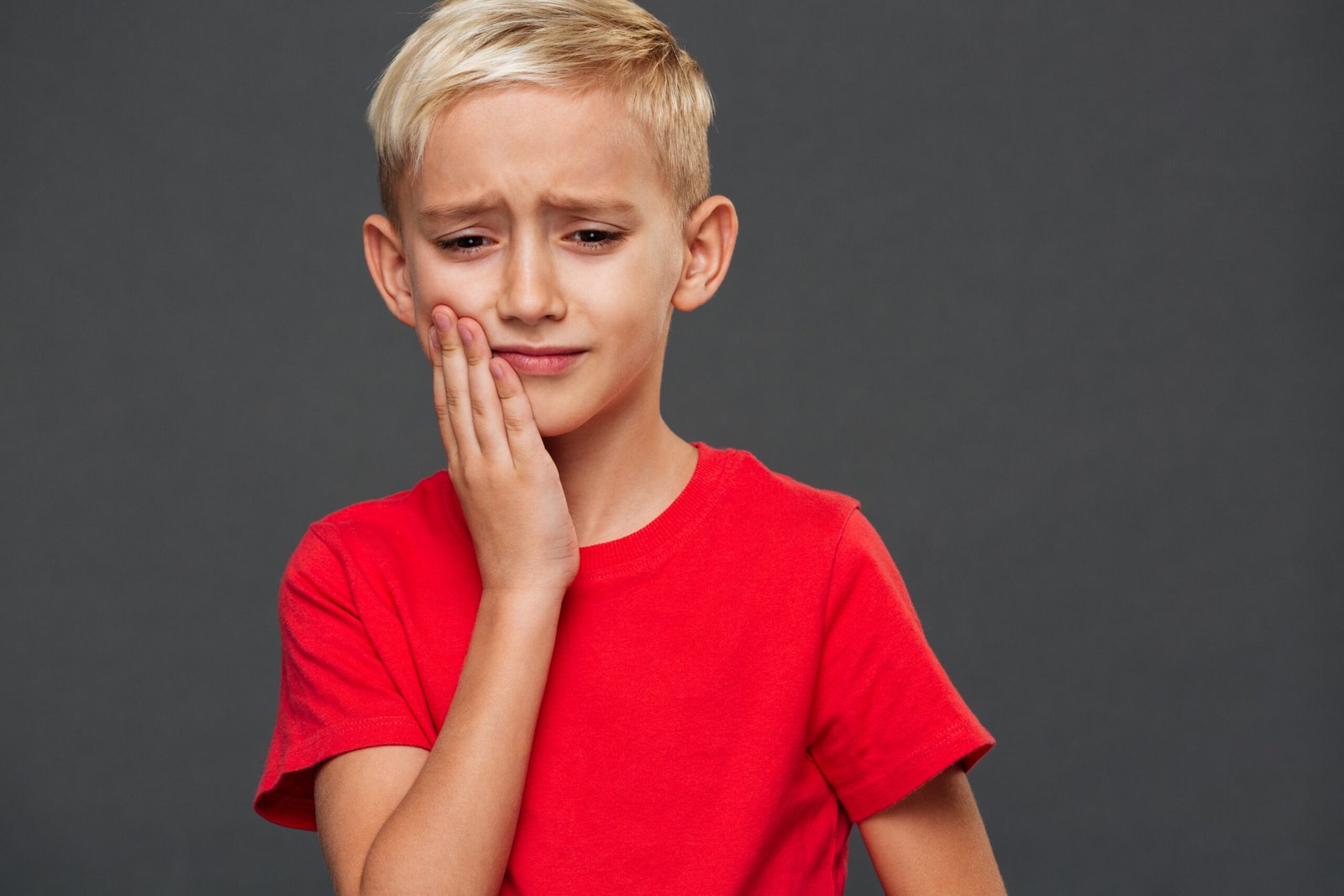 A boy holding his cheek in pain, showing signs of a toothache representing Children's Dental Emergencies in Beverly Hills.